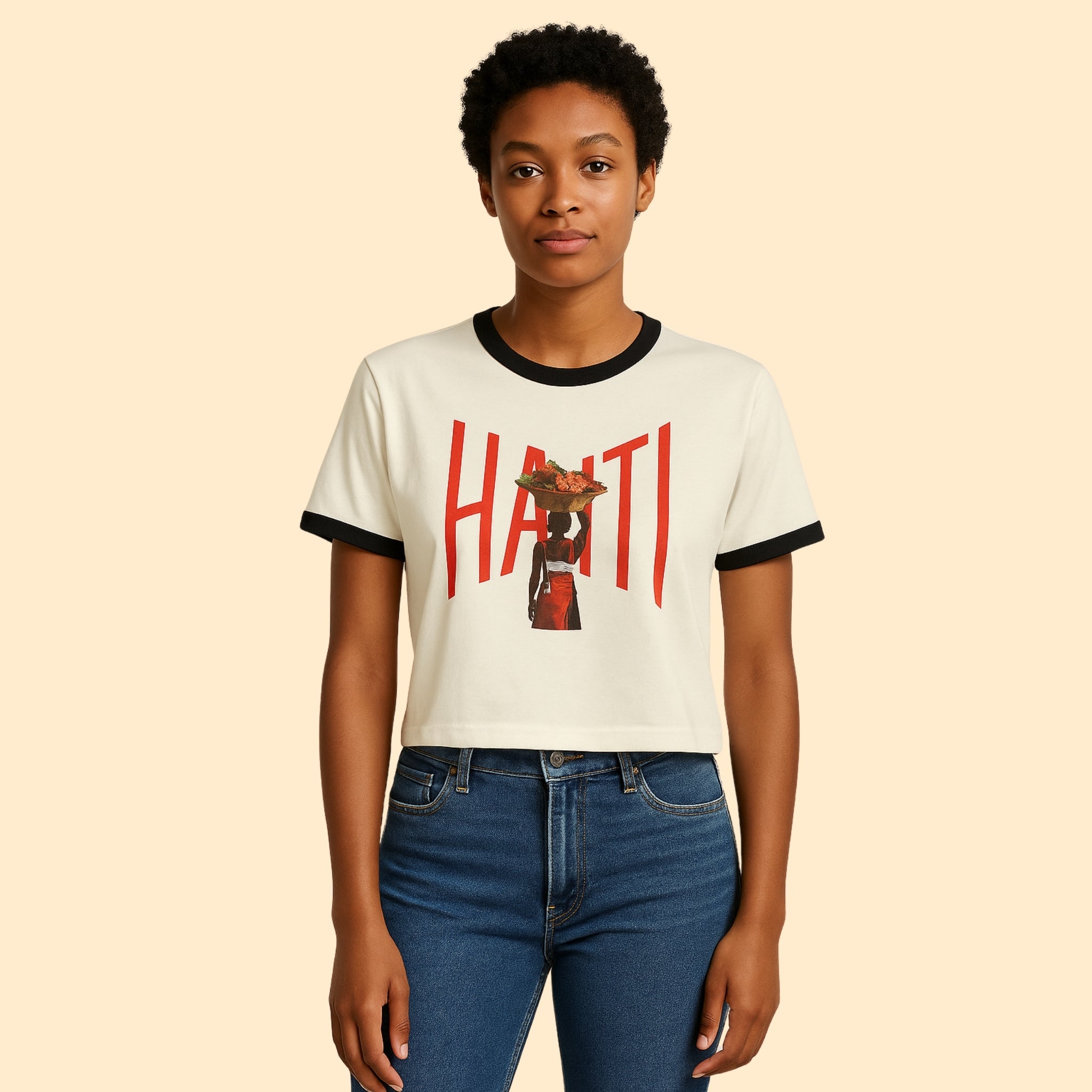 Model wearing Breakin' Atoms "Heritage Pride Ringer Tee – Haitian Beauty Edition," a cropped off-white tee with black collar and sleeve trim, featuring bold red "HAITI" lettering and silhouette graphic of a Haitian woman in traditional attire.