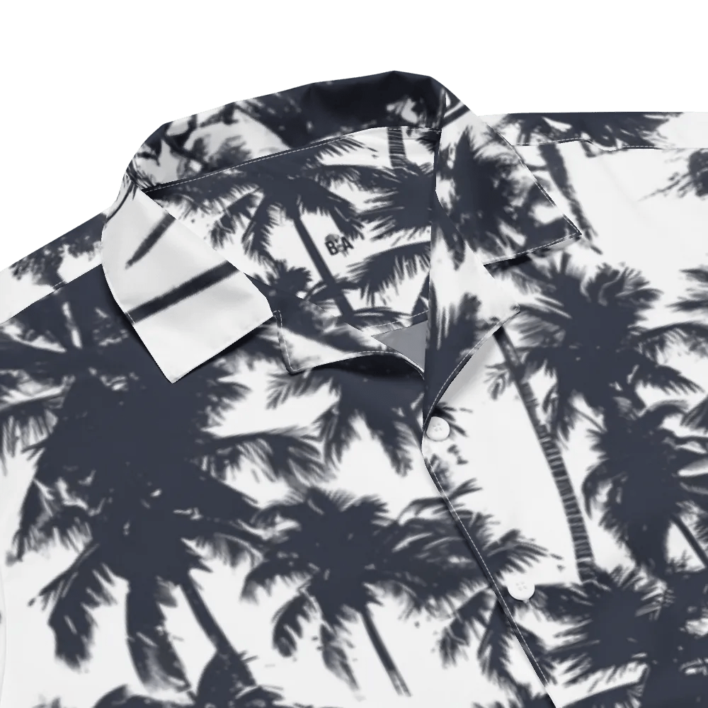 Model wearing Breakin' Atoms "Monochrome Palm Shadow Button-Up," a short sleeve tropical shirt with all-over black palm tree silhouettes on a white background — perfect for vacation or summer streetwear.