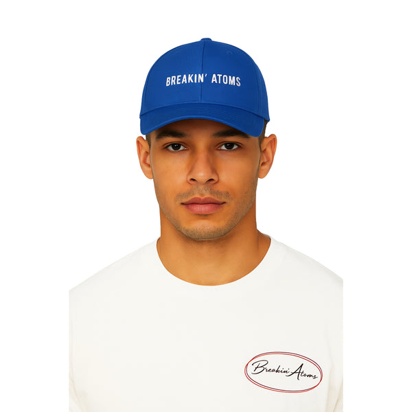 Model wearing the Breakin' Atoms "Minimal Hat" in royal blue — a clean, structured baseball cap with white embroidered Breakin' Atoms logo, blending simplicity, function, and streetwear identity.